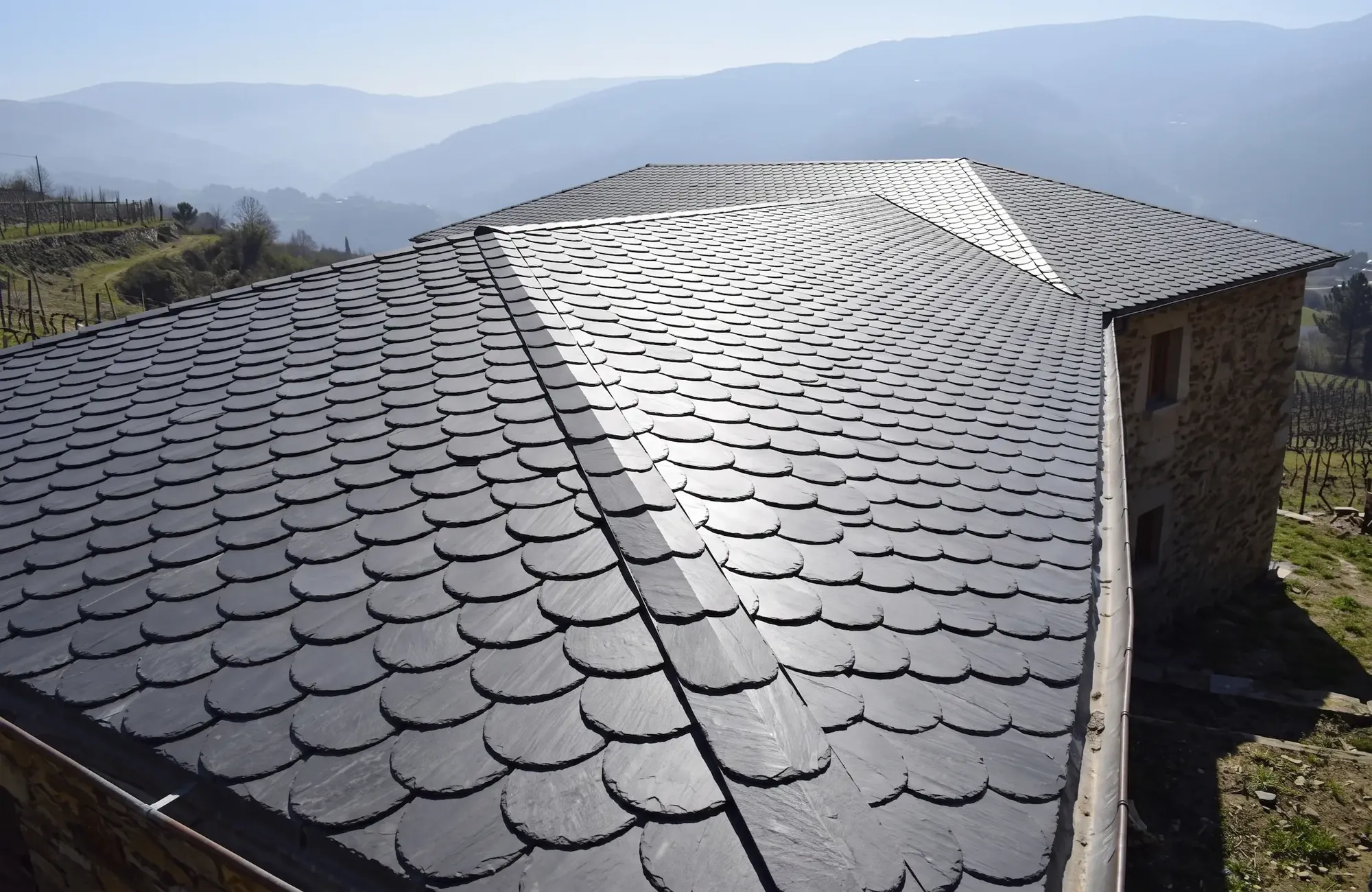Scalloped natural slate roof on a stone house, mountain valley behind